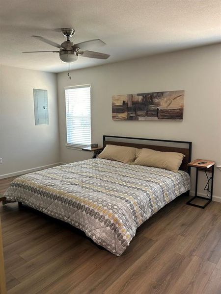 Bedroom featuring ceiling fan, a textured ceiling, hardwood / wood-style flooring, and electric panel