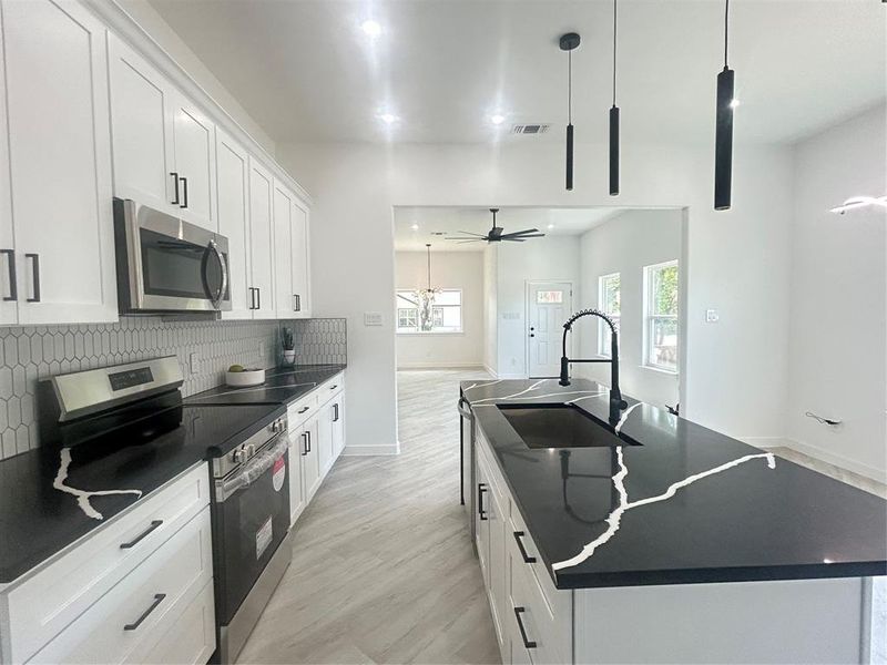 Kitchen featuring range, light wood-type flooring, backsplash, a kitchen island with sink, and ceiling fan