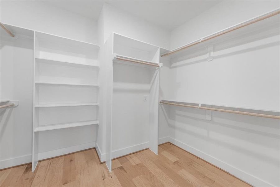 Step into your spacious, clean-lined owners retreat dressed walk-in closet featuring built-in white shelving on one side and multiple hanging rods for ample clothing storage.