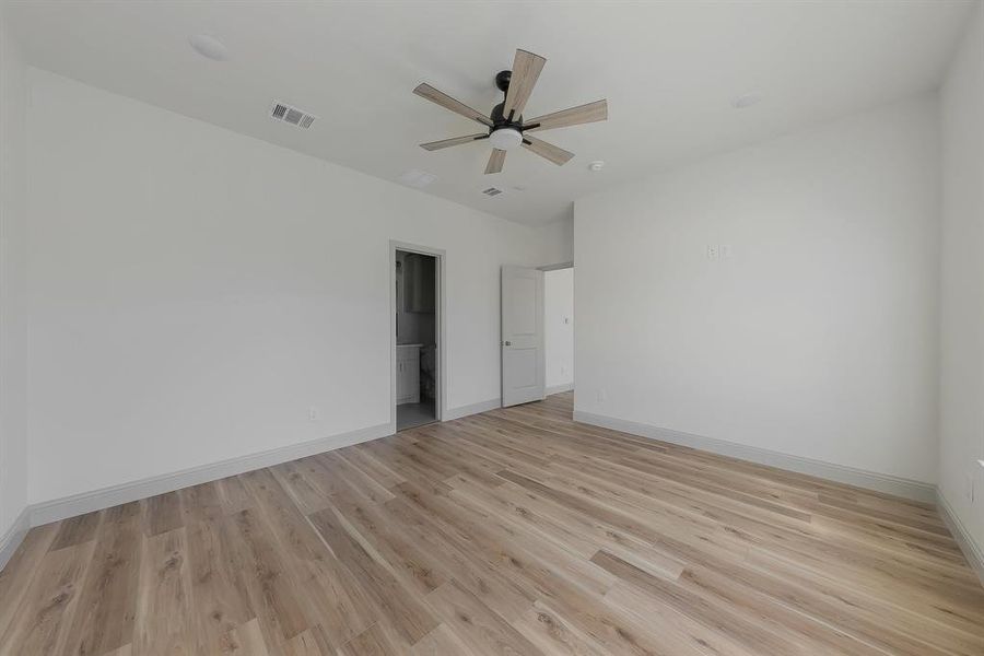 Unfurnished bedroom featuring a spacious closet, a closet, light hardwood / wood-style floors, and ceiling fan