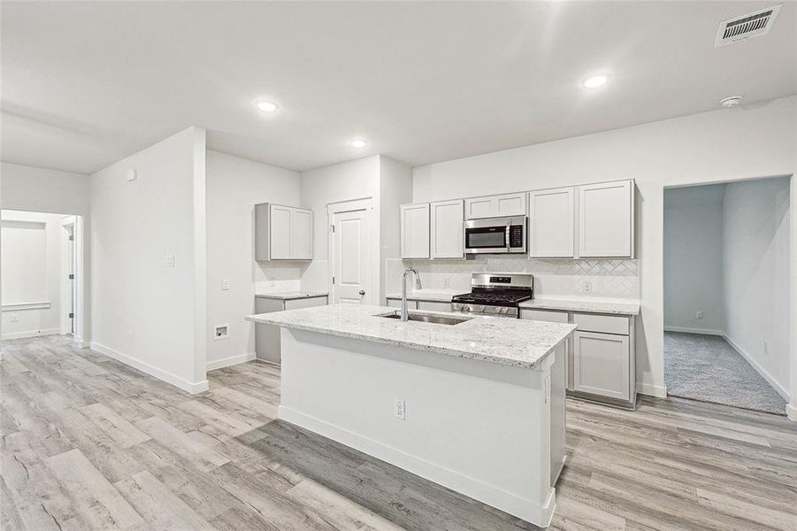 Kitchen with appliances with stainless steel finishes, sink, light hardwood / wood-style floors, decorative backsplash, and a kitchen island with sink