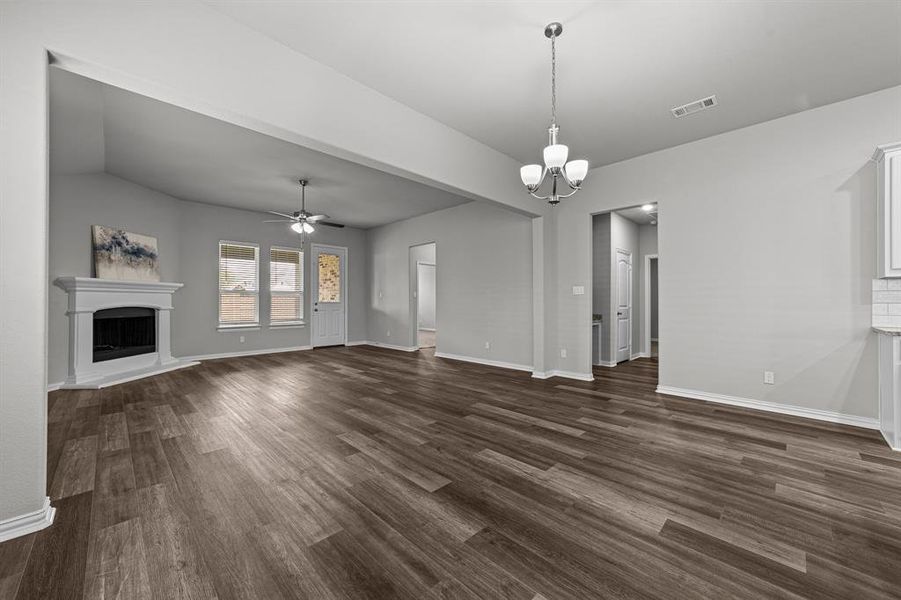 Unfurnished living room featuring ceiling fan with notable chandelier, dark wood-type flooring, and lofted ceiling