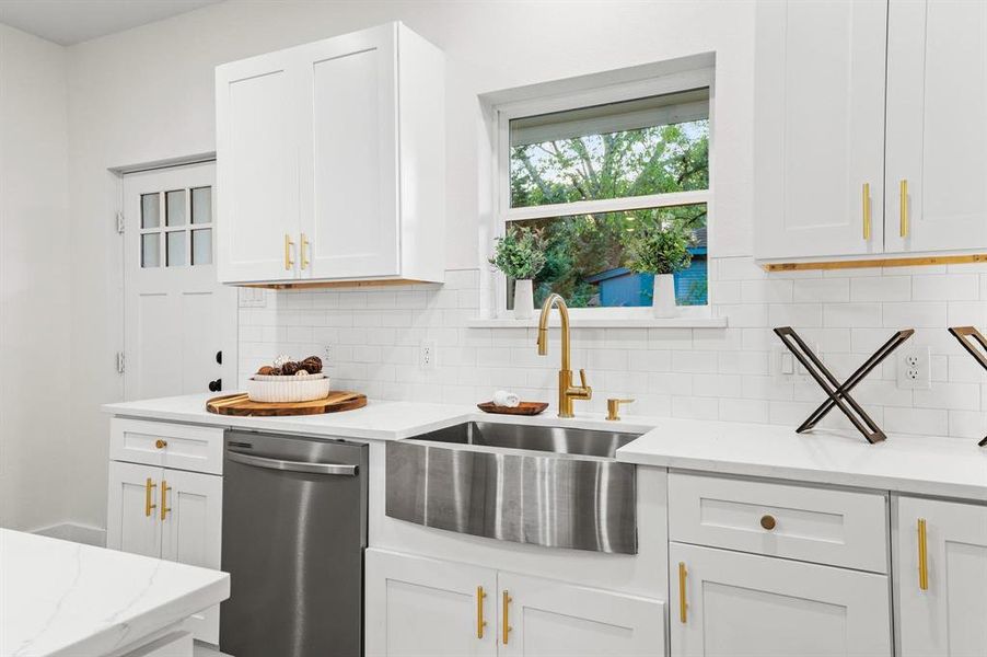 Kitchen with dishwasher, sink, light stone countertops, white cabinets, and tasteful backsplash