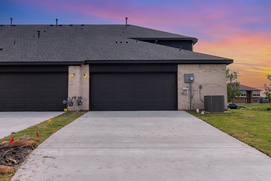 View of front of house featuring a garage, central air condition unit, and a yard