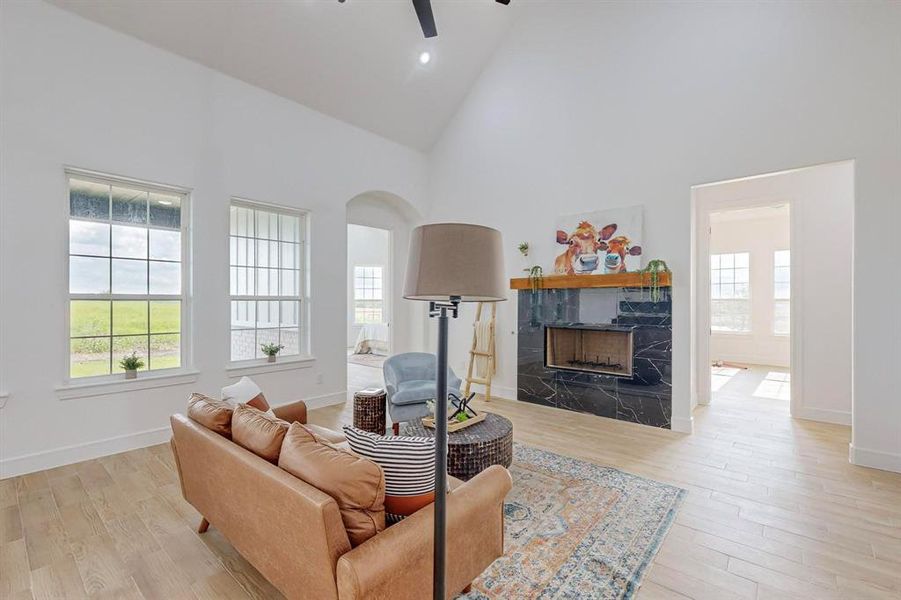 Living room featuring light hardwood / wood-style floors, a premium fireplace, ceiling fan, and high vaulted ceiling