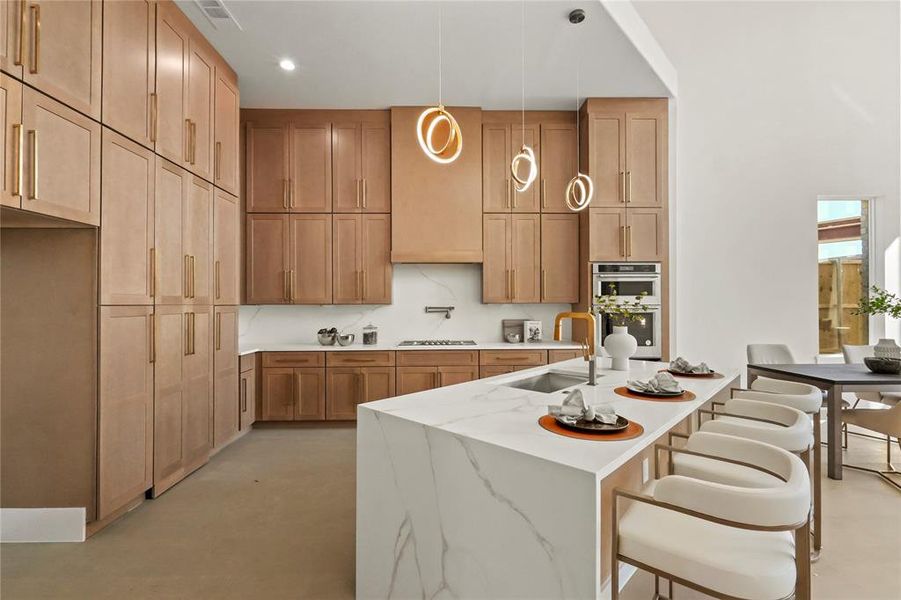 Kitchen featuring stovetop, double oven, sink, pendant lighting, and light stone counters