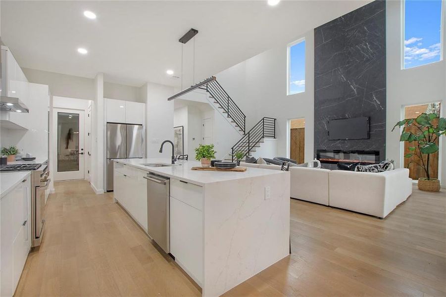 Kitchen with appliances with stainless steel finishes, sink, hanging light fixtures, white cabinetry, and a center island with sink