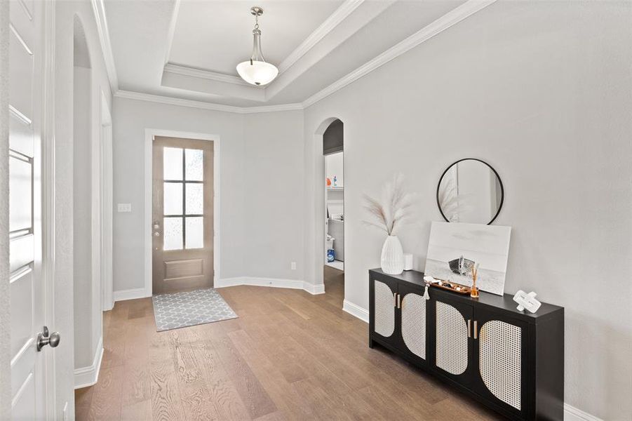 Foyer with ornamental molding, a tray ceiling, and hardwood / wood-style floors