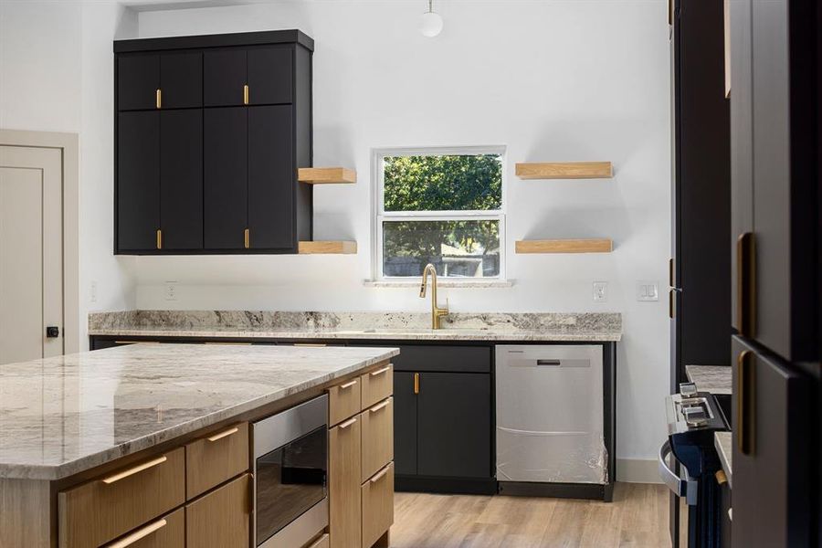 Kitchen with light stone countertops, stainless steel appliances, sink, light hardwood / wood-style flooring, and a kitchen island