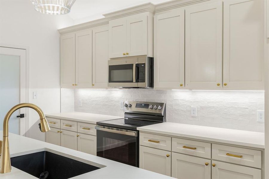 Kitchen with decorative backsplash, stainless steel appliances, white cabinetry, and sink