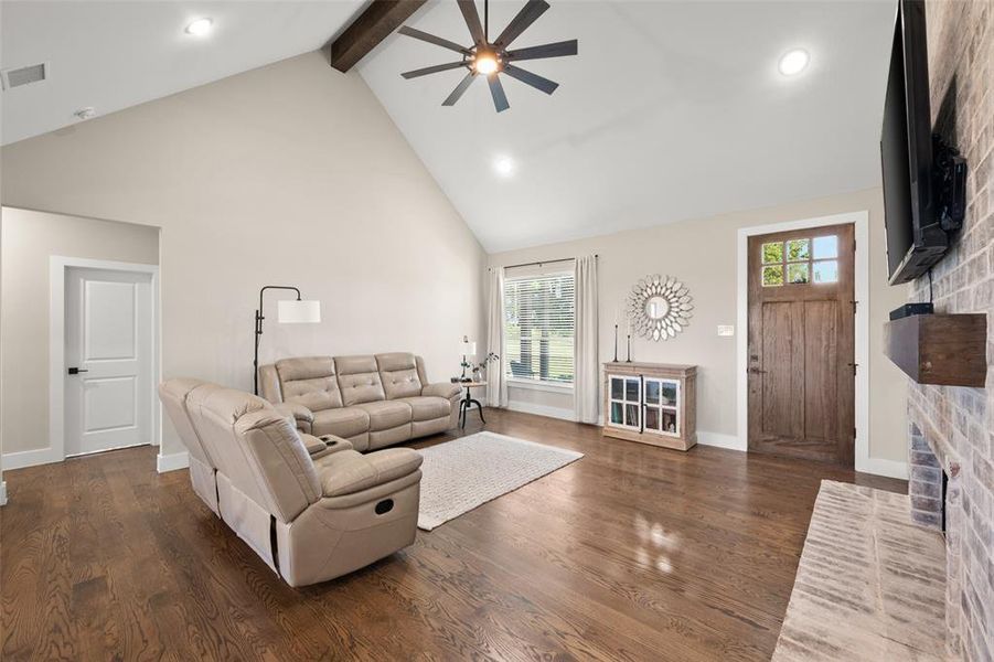 Living room featuring dark hardwood floors, ceiling fan, beamed ceiling, a fireplace, and high vaulted ceiling