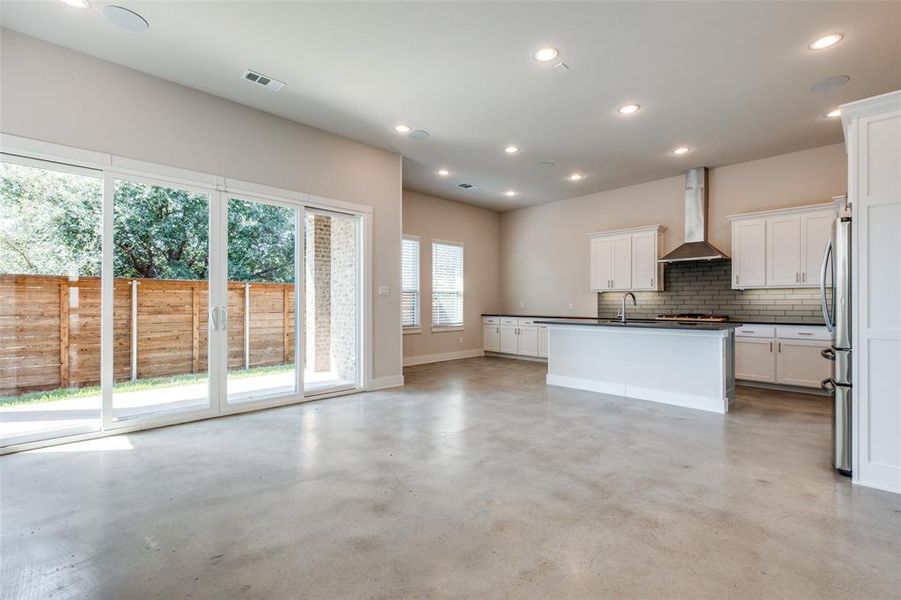 Kitchen featuring wall chimney exhaust hood, an island with sink, sink, white cabinetry, and stainless steel refrigerator