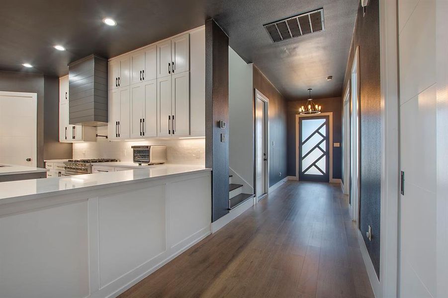 Kitchen featuring gas stove, white cabinets, decorative light fixtures, and dark wood-type flooring