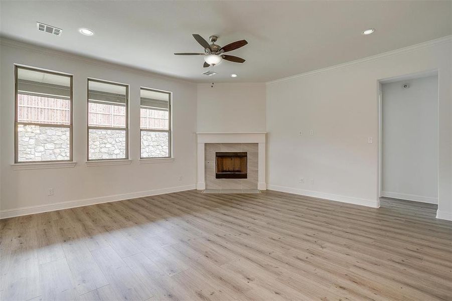 Unfurnished living room featuring ornamental molding, a tiled fireplace, ceiling fan, and light wood-type flooring