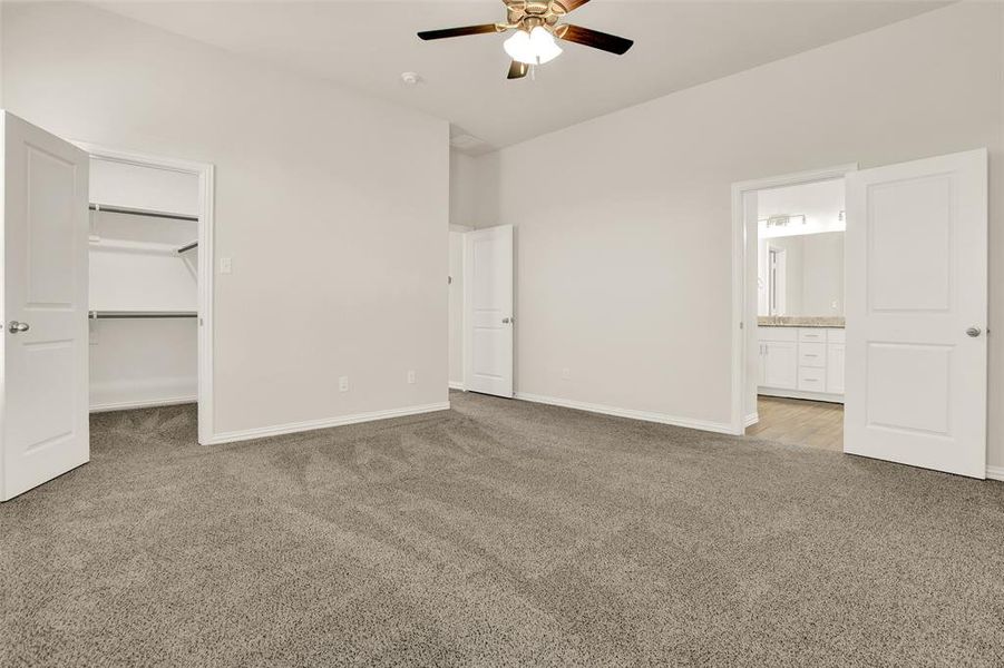 Unfurnished bedroom featuring light carpet, a walk in closet, connected bathroom, and ceiling fan