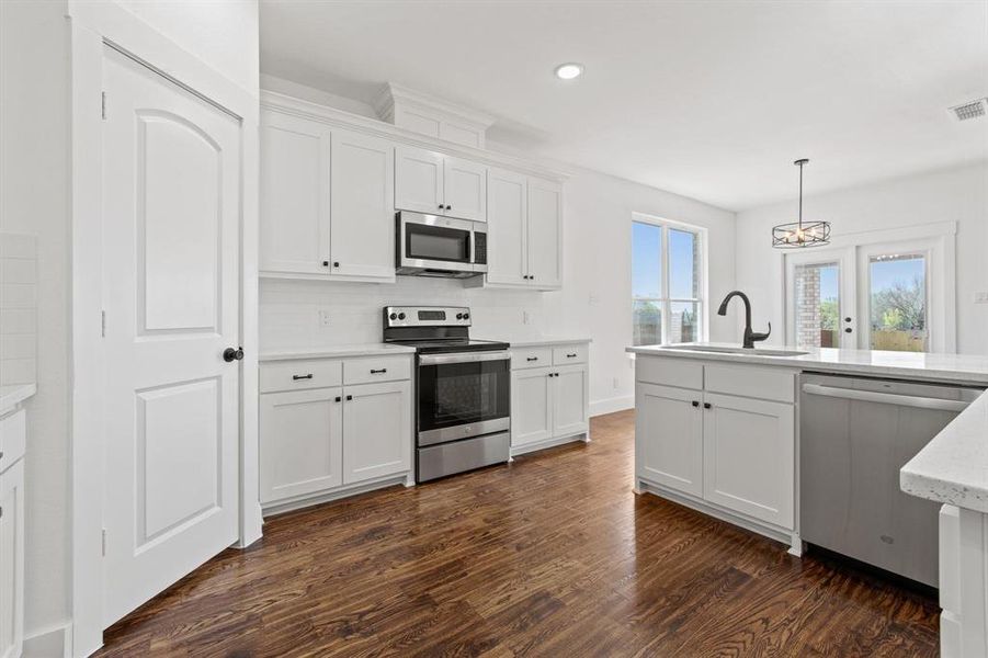 Kitchen featuring sink, white cabinetry, stainless steel appliances, decorative light fixtures, and dark hardwood / wood-style flooring