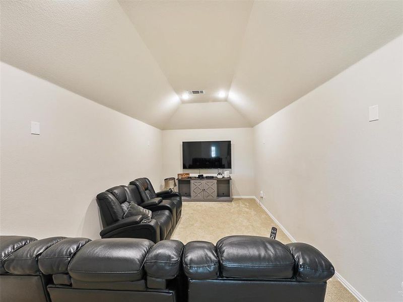 Home theater featuring light colored carpet and vaulted ceiling