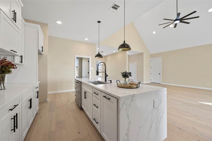 Kitchen featuring a center island with sink, light stone counters, white cabinetry, light wood-type flooring, and sink