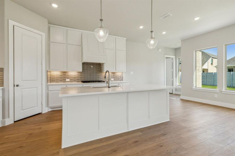 Kitchen featuring white cabinets, sink, an island with sink, pendant lighting, and light wood-type flooring