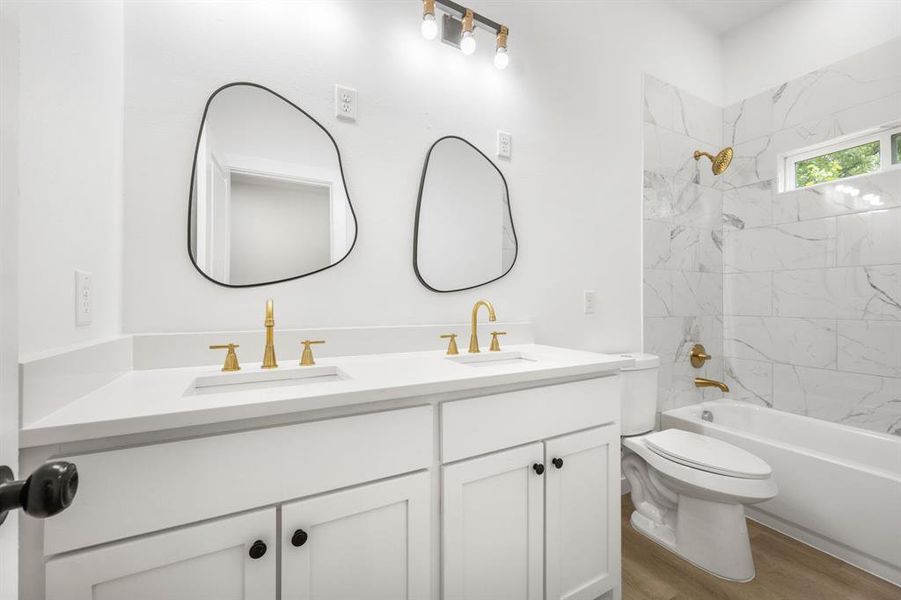 Full bathroom featuring hardwood / wood-style floors, tiled shower / bath, dual bowl vanity, and toilet