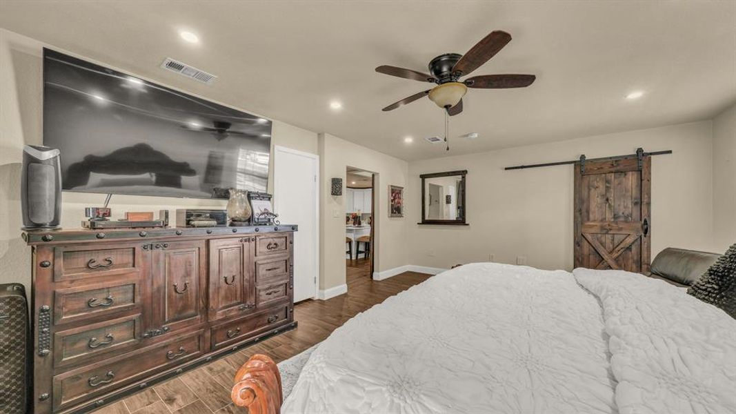 Bedroom with a barn door, ceiling fan, and dark hardwood / wood-style flooring