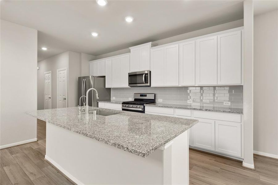 This light and bright kitchen features a large quartz island, white cabinets, a large sink overlooking your family room, recessed lighting, and beautiful backsplash.