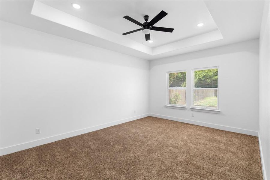 Empty room with carpet, ceiling fan, and a tray ceiling