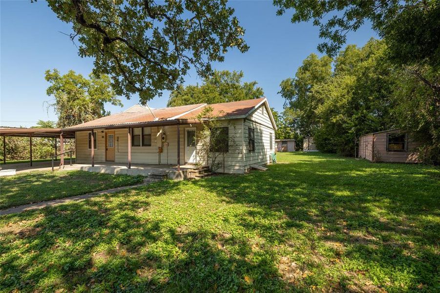 Back of house featuring a porch, a yard, and a carport