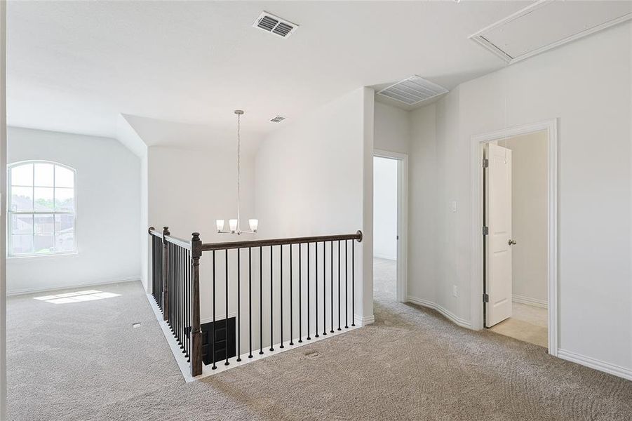 Corridor featuring lofted ceiling, light carpet, and a notable chandelier