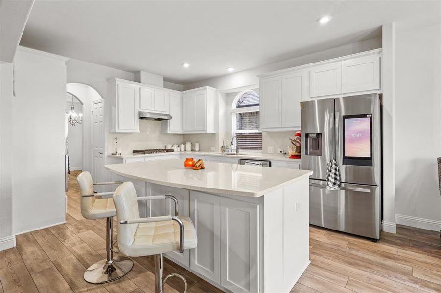 Kitchen featuring light hardwood / wood-style floors, a center island, stainless steel fridge with ice dispenser, white cabinetry, and a kitchen bar