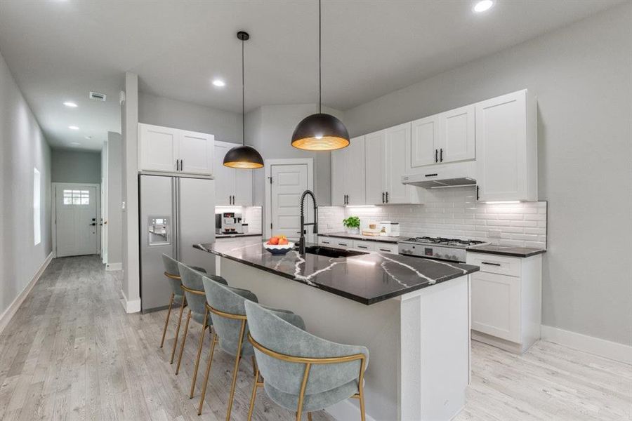 Kitchen featuring sink, refrigerator with ice dispenser, light wood-type flooring, and a center island with sink