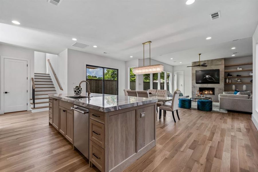 Kitchen featuring a large fireplace, stainless steel dishwasher, light wood-type flooring, built in features, and a kitchen island with sink
