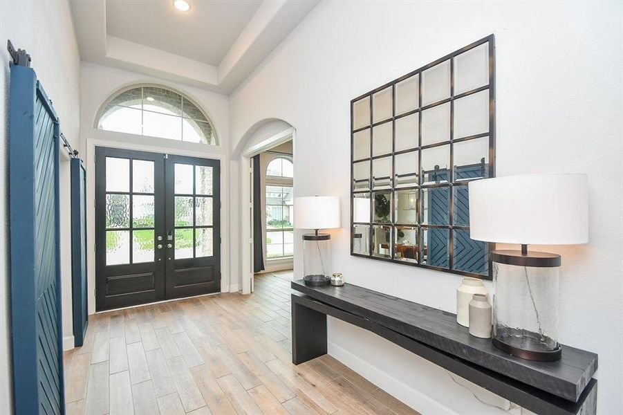 This is a bright and welcoming entryway with high ceilings, featuring a modern front door with glass panels, and a unique barn-style sliding door to dining room.