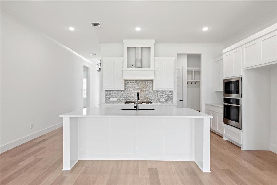 Kitchen with built in microwave, white cabinetry, oven, and light wood-type flooring