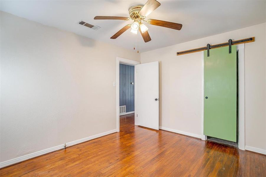 Unfurnished bedroom with dark wood-type flooring, ceiling fan, and a barn door