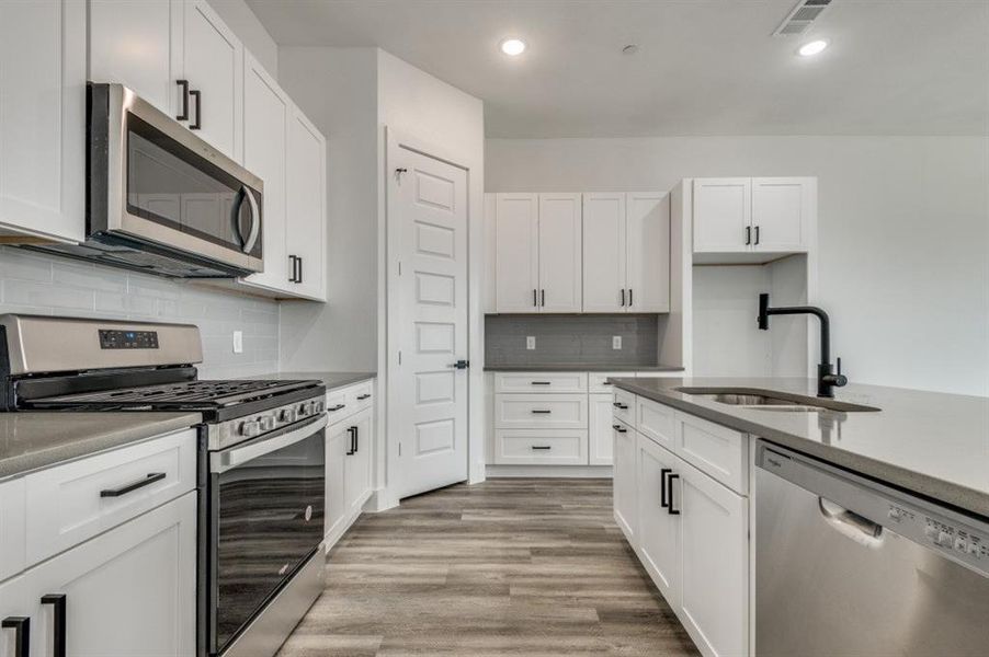 Kitchen with stainless steel appliances, white cabinets, sink, tasteful backsplash, and light wood-type flooring