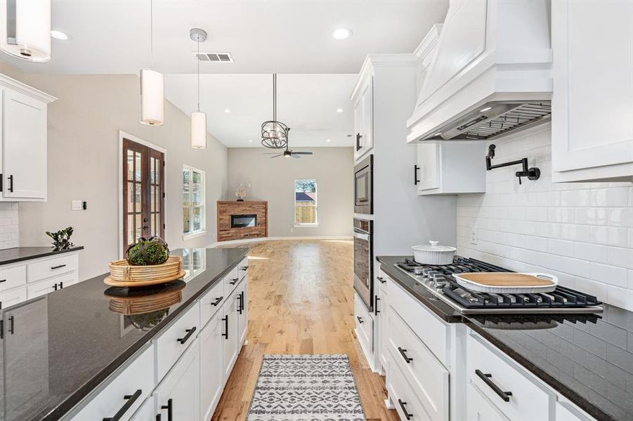 Kitchen with pendant lighting, tasteful backsplash, light hardwood / wood-style flooring, white cabinetry, and custom range hood