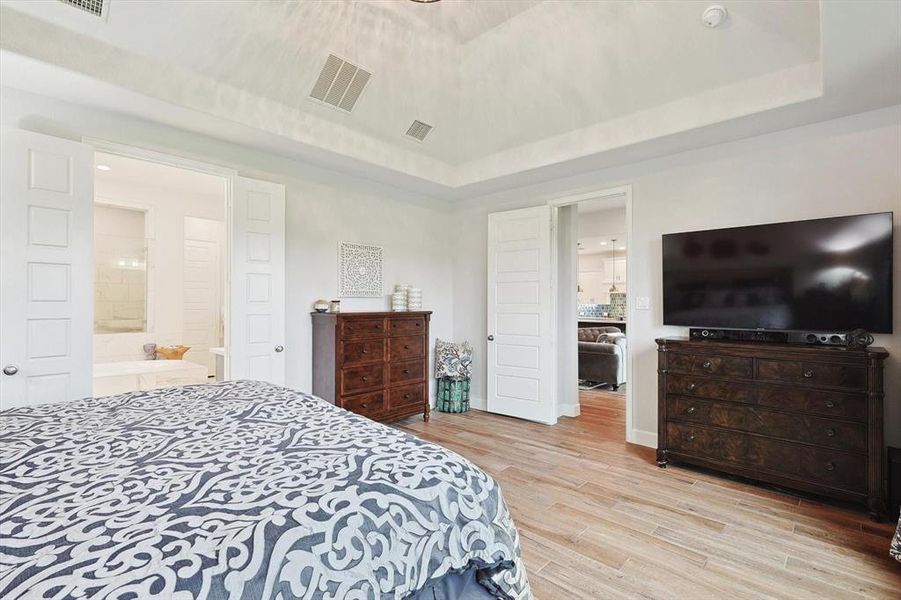 Bedroom featuring light wood-type flooring, a tray ceiling, and connected bathroom