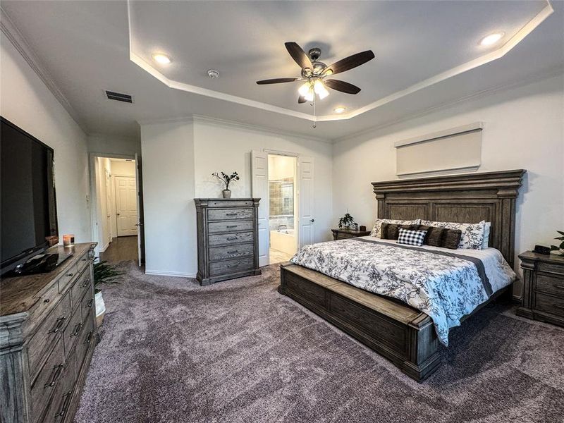 Bedroom with ensuite bath, a raised ceiling, ceiling fan, dark colored carpet, and ornamental molding