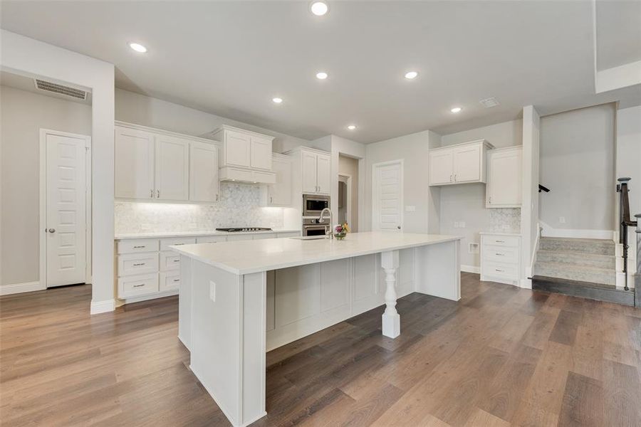 Kitchen with decorative backsplash, white cabinets, stainless steel appliances, hardwood / wood-style floors, and a spacious island