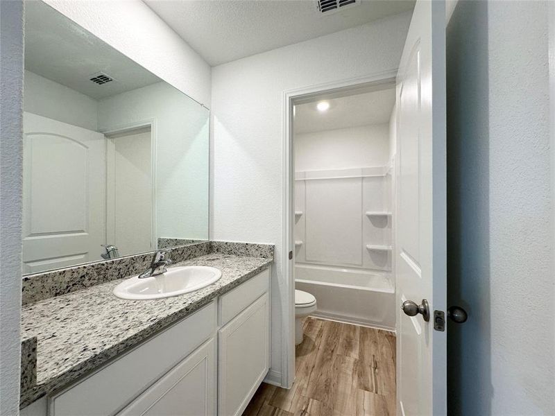 Secondary bathroom includes granite counters, designer white cabinetry and luxury vinyl plank flooring.