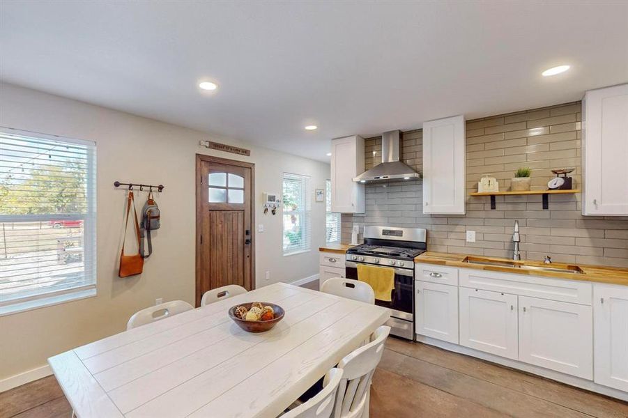 Kitchen with tasteful backsplash, sink, white cabinetry, wall chimney exhaust hood, and gas range