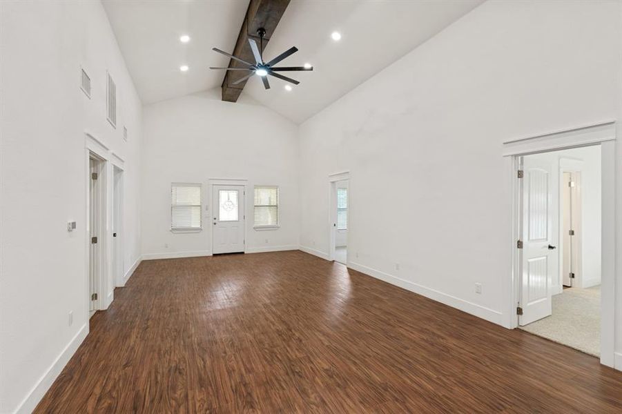 Unfurnished living room featuring cedar beamed ceiling, dark hardwood / wood-style floors, ceiling fan, and high vaulted ceiling