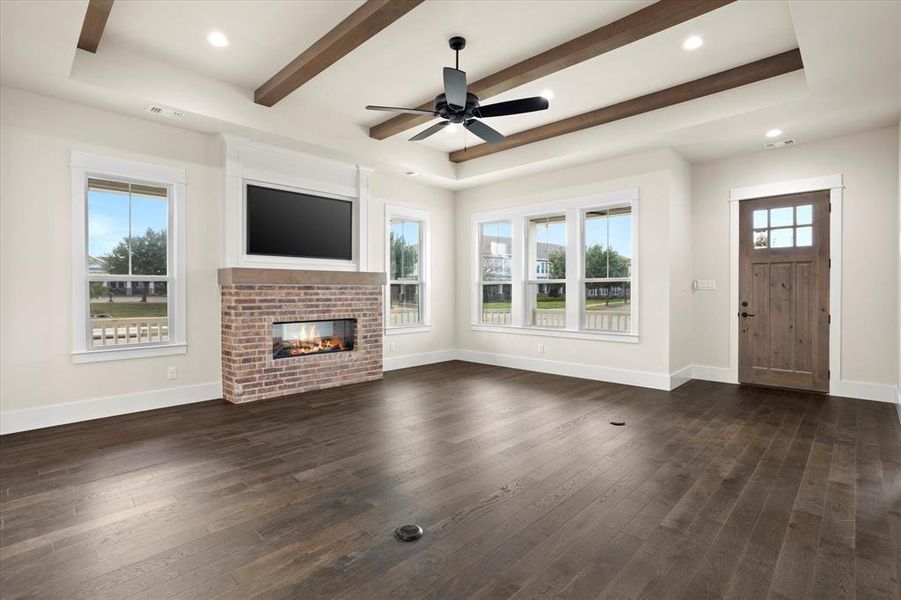 Unfurnished living room featuring a brick fireplace, beam ceiling, ceiling fan, and dark hardwood / wood-style floors