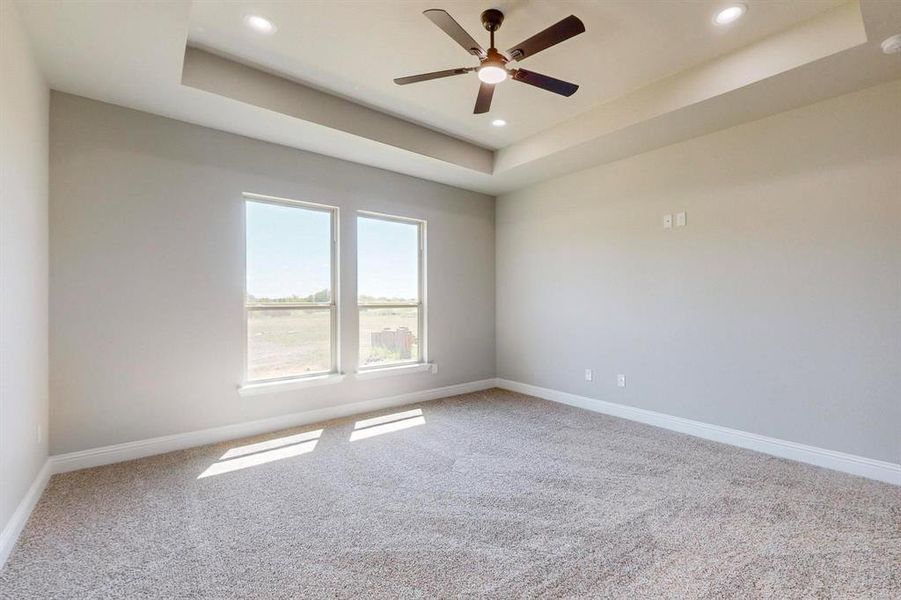 Carpeted empty room featuring ceiling fan and a tray ceiling