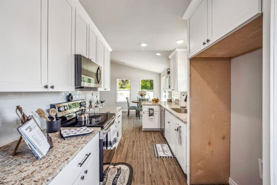 Kitchen with light stone countertops, white cabinets, vaulted ceiling, and appliances with stainless steel finishes