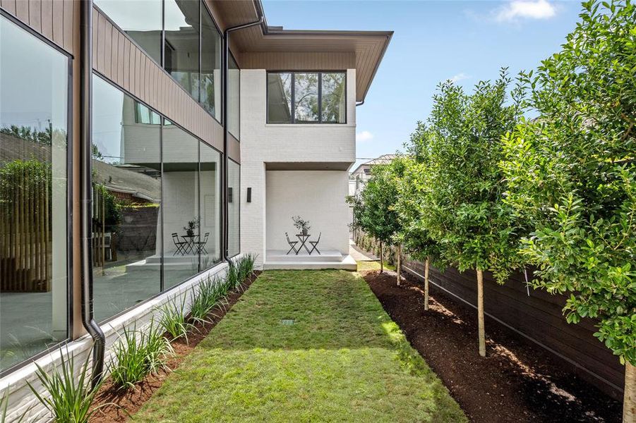 This charming side yard features a beautifully landscaped lawn bordered by neatly planted trees, providing a tranquil outdoor space.