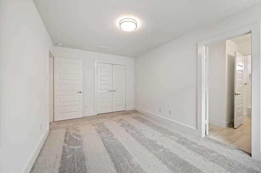 Unfurnished bedroom with connected bathroom, light colored carpet, and a closet