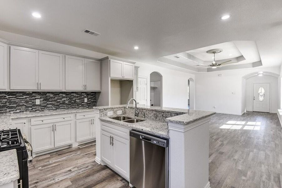 Kitchen with black gas stove, a center island with sink, sink, stainless steel dishwasher, and white cabinetry