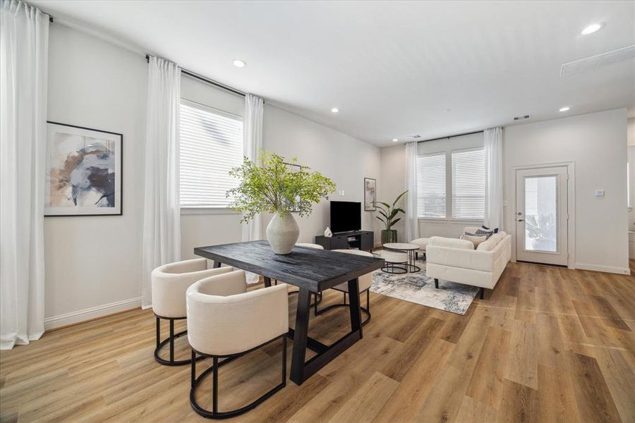 The open-concept layout extends seamlessly from the living area into the dining space, creating a functional flow perfect for entertaining. Large windows provide natural light, enhancing the warmth of the light-colored flooring. The sliding door offers easy access to outdoor spaces, adding to the home's inviting atmosphere.